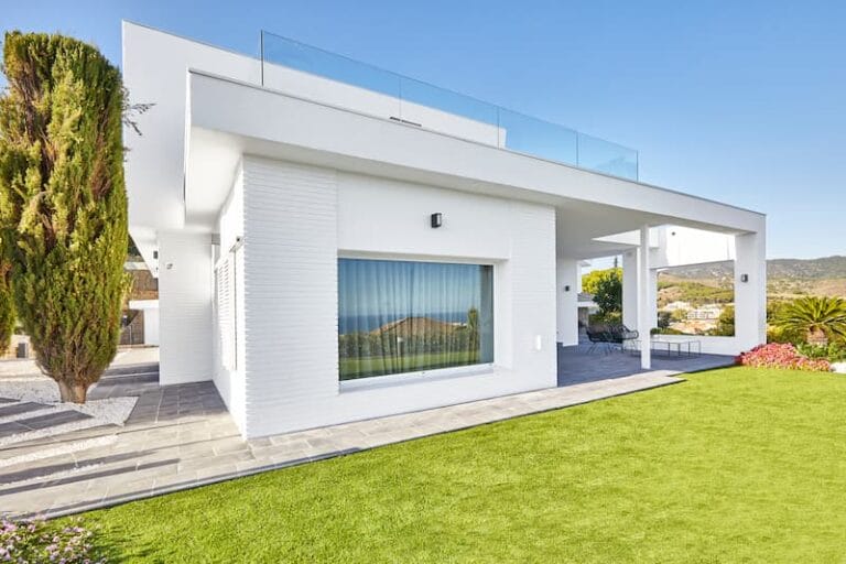 Vivienda blanca de una planta con cubierta plana, grandes ventanales y jardín