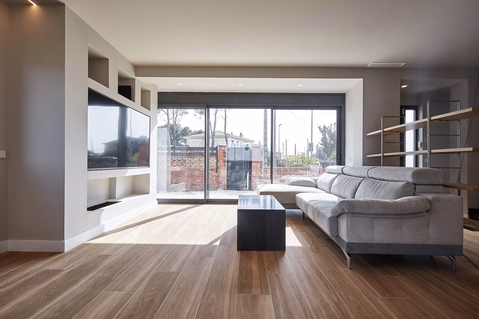 Salón con sofá gris y gran ventanal hacia la terraza