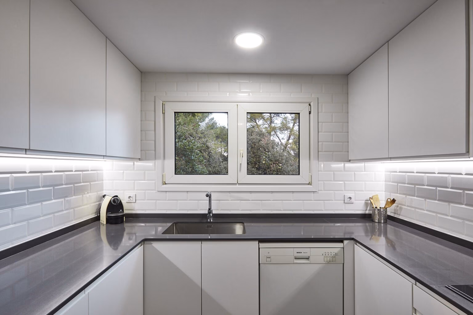 Cocina blanca con fregadero bajo ventana y encimera oscura