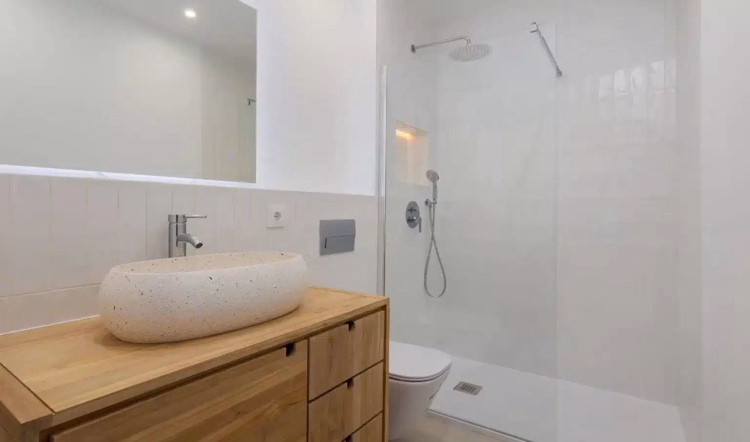 Lavabo ovalado sobre mueble de vetas visibles y ducha