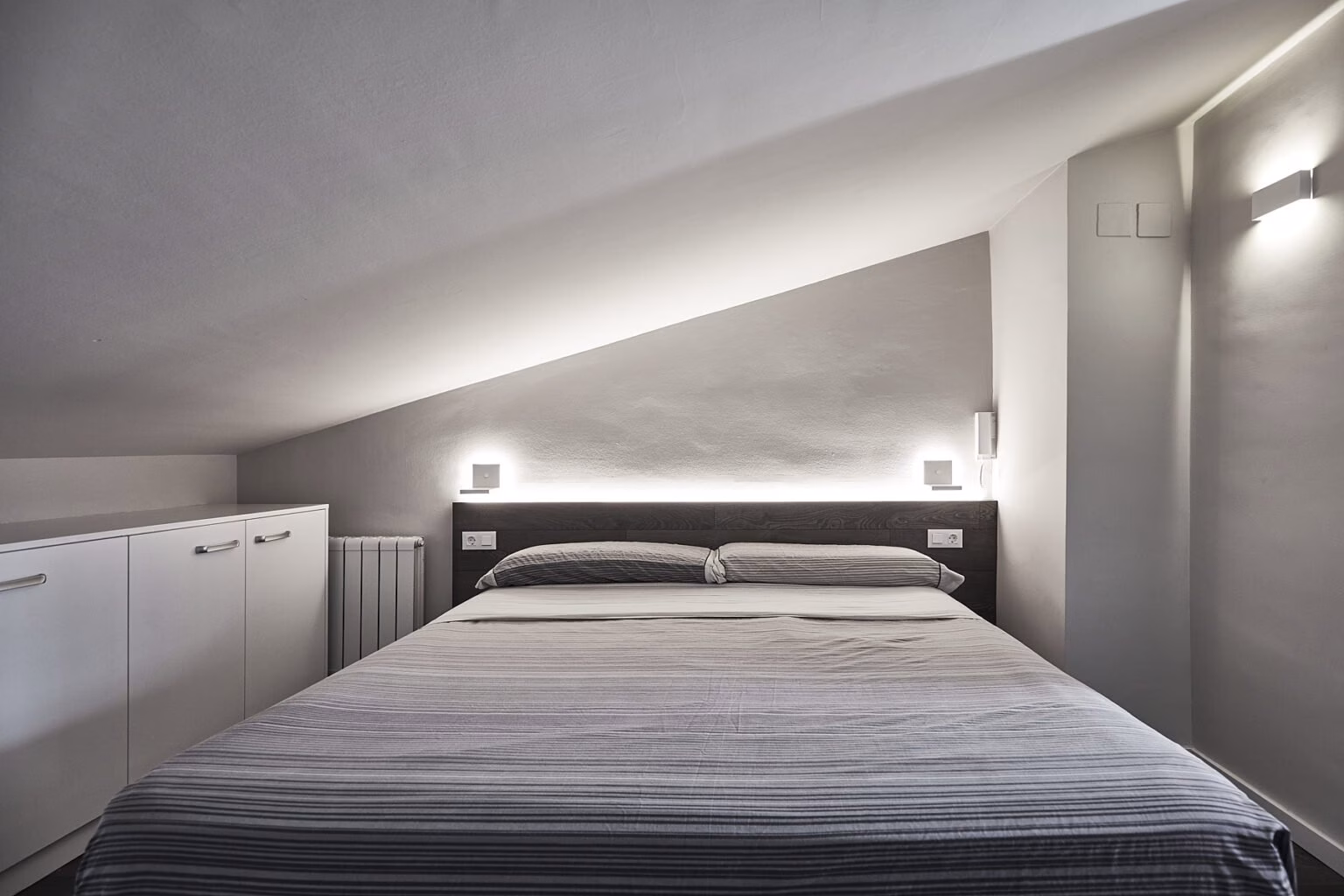 Dormitorio bajo techo inclinado con cabecero oscuro