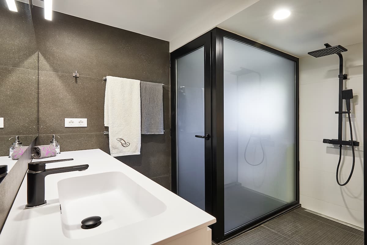 Baño con lavabo blanco, grifería negra y cerramiento translúcido