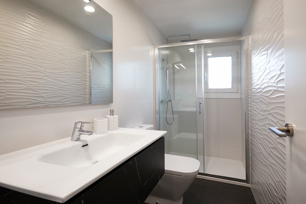 Baño blanco con pared de relieve y mueble oscuro