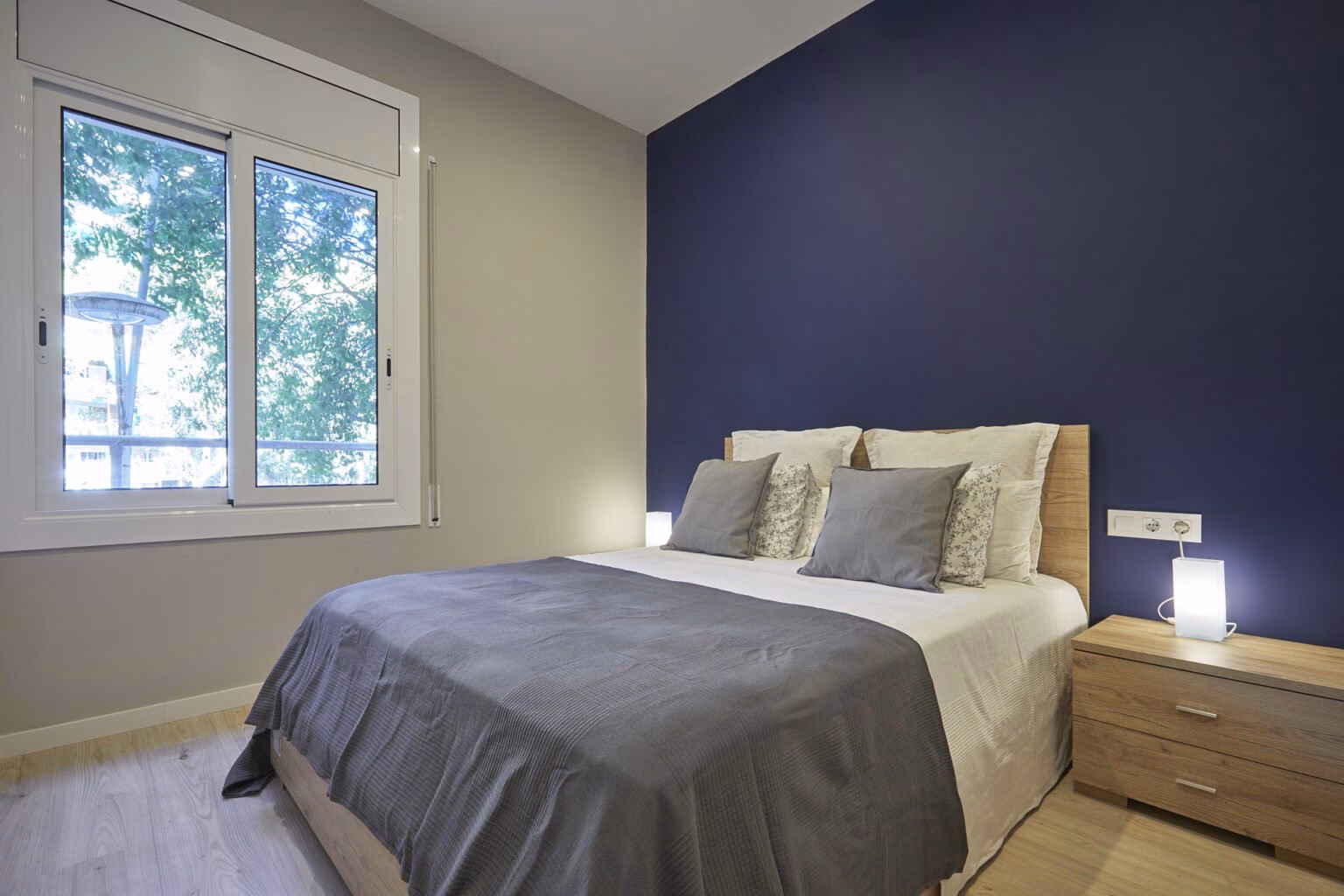Dormitorio con pared azul y mesilla de tono madera