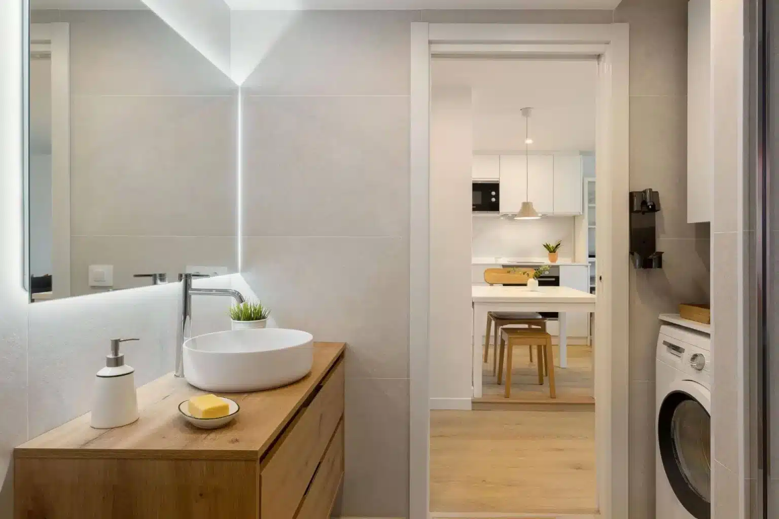 Lavabo blanco sobre mueble cálido junto a paso hacia cocina