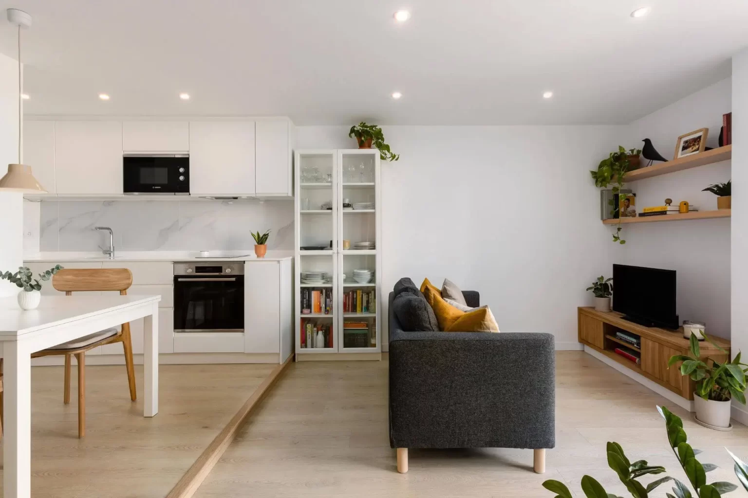 Sofá gris entre cocina blanca y mueble de televisión
