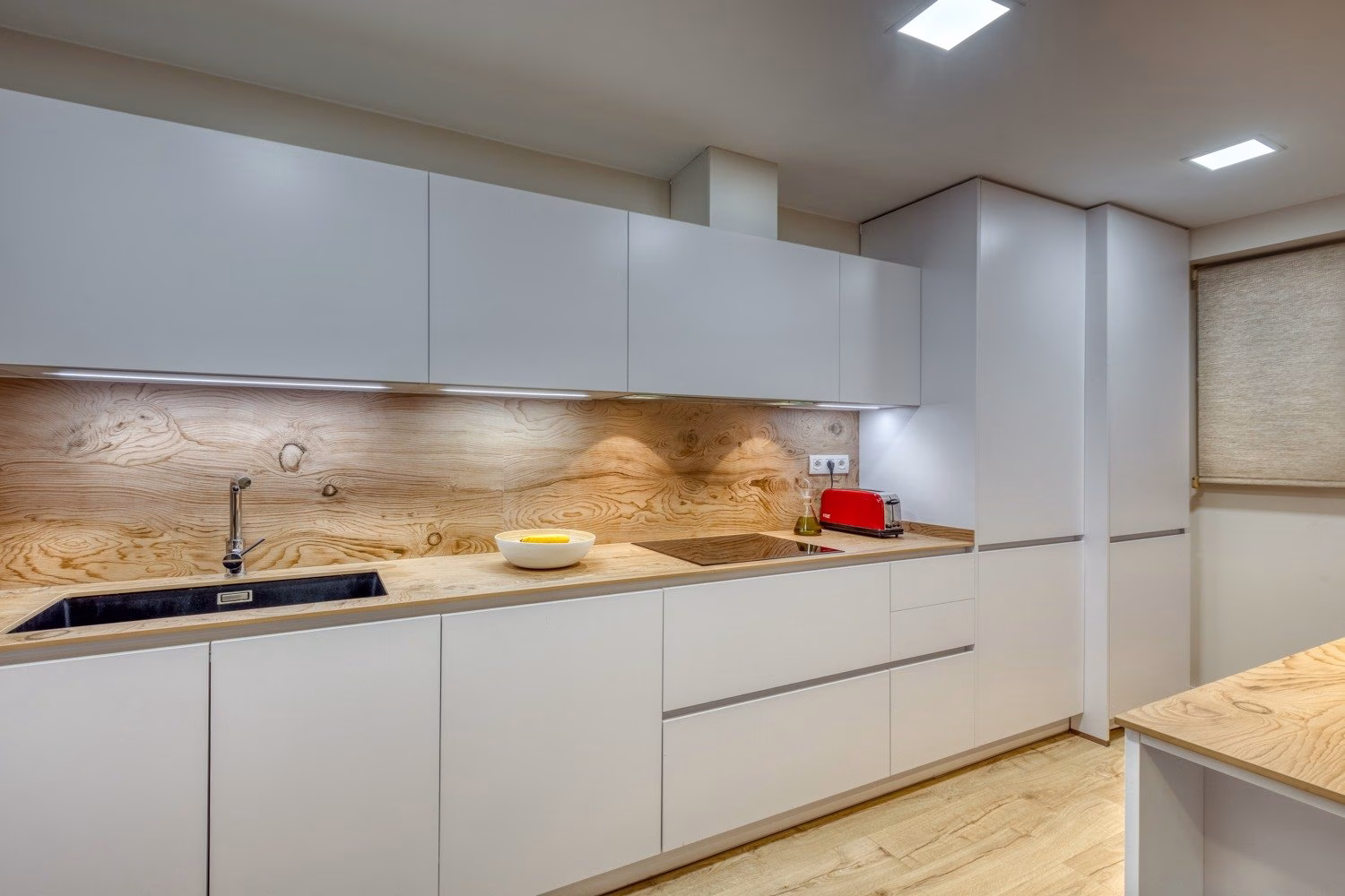 Cocina lineal con armarios blancos y encimera de tono madera