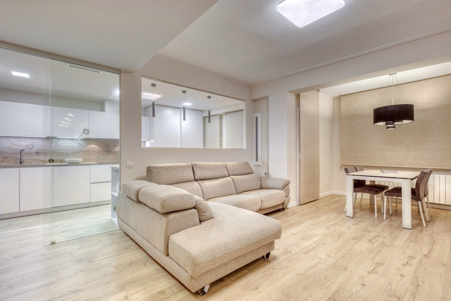 Salón con sofá beige junto a cocina acristalada