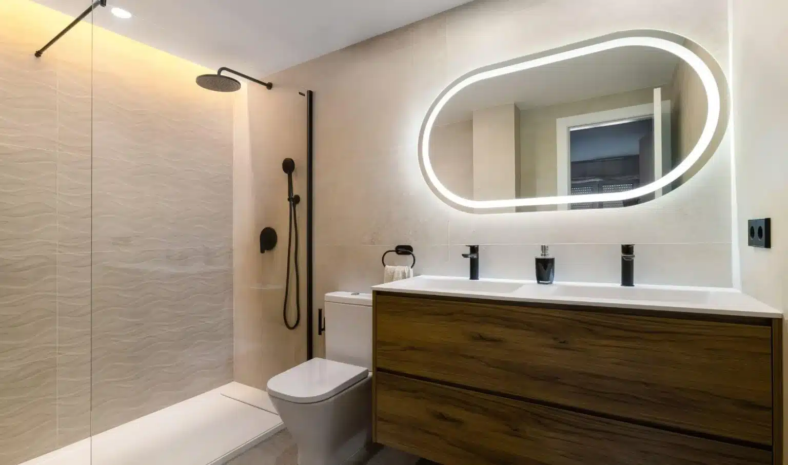 Baño con espejo de contorno redondeado y ducha transparente