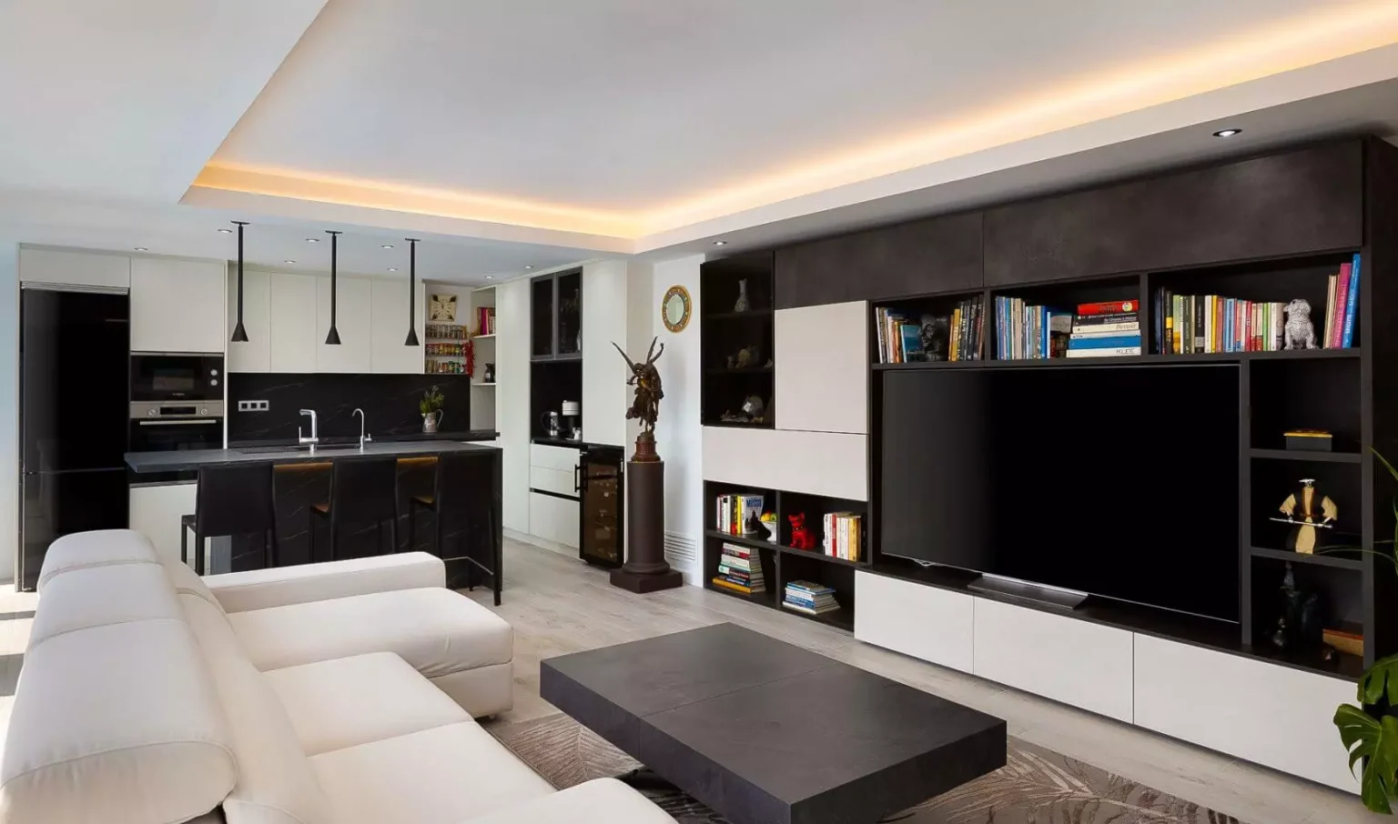 Salón blanco con mueble de televisión negro y cocina abierta